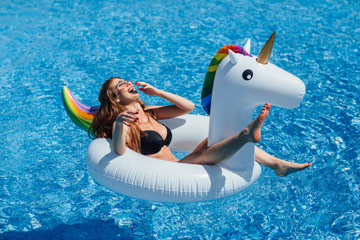 Young beautiful brown-haired girl with a good figure tan in the pool on an inflatable unicorn in a black swimsuit.